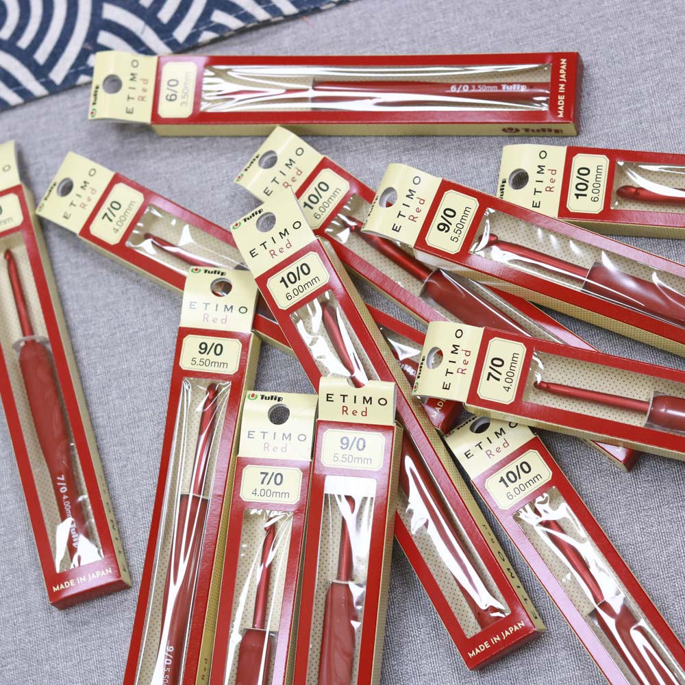 許多盒裝的紅色Tulip Etimo鉤針散落在桌上，展示其精美的包裝和專業的質感。