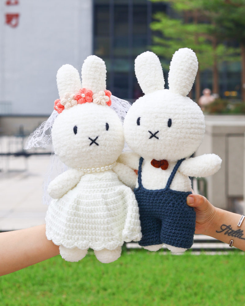 一對用白色毛絨線鉤織的Miffy結婚玩偶。左邊是穿著白色婚紗、戴著花冠的新娘Miffy；右邊是穿著深藍色吊帶褲、戴著領結的新郎Miffy。