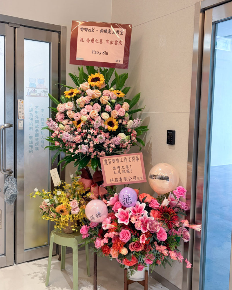 唧唧鉤織創意教室新工作室門口擺放著兩個精美的祝賀花牌，上方分別寫著「祝 喬遷之喜 客似雲來」與「慶賀唧唧工作室開幕 喬遷之喜！大展鴻圖！」，旁邊還有寫著「祝爆賺」的可愛氣球。