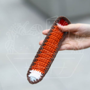 Crocheted orange-and-brown bookmark held by a person, with a small white-and-blue tip at the end.