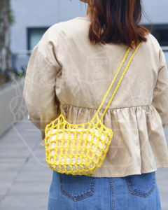 Back view of a person wearing a beige jacket and blue jeans, carrying a bright yellow crocheted crossbody bag.