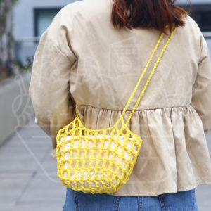 Back view of a person wearing a beige jacket and blue jeans, carrying a bright yellow crocheted crossbody bag.