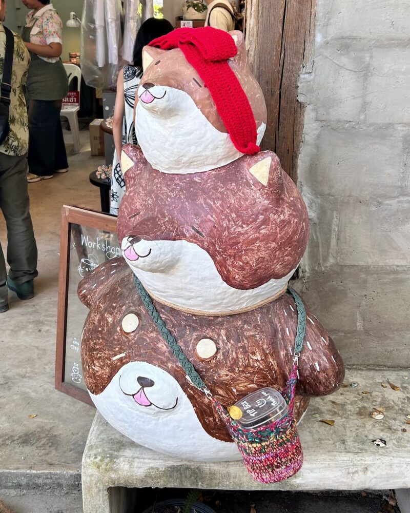 店門旁疊放三隻啡白色動物造型擺設，最上方戴著紅色鉤織蝴蝶結，最下方掛著彩色鉤織杯袋，袋內放有飲品杯。